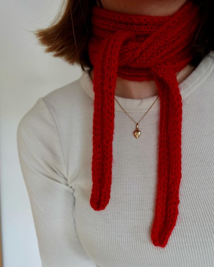 a woman wearing a red scarf with a gold heart charm on it's neck