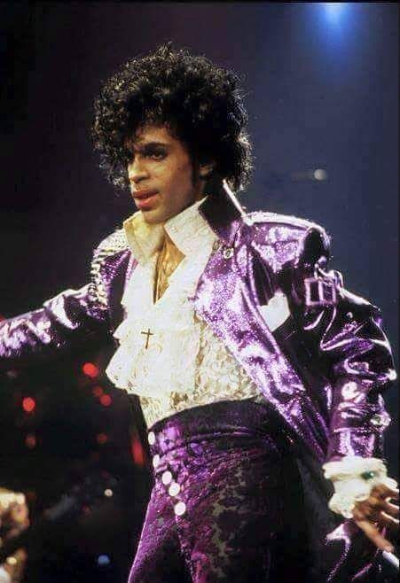 prince performing on stage in purple pants and white shirt with his hands out to the side