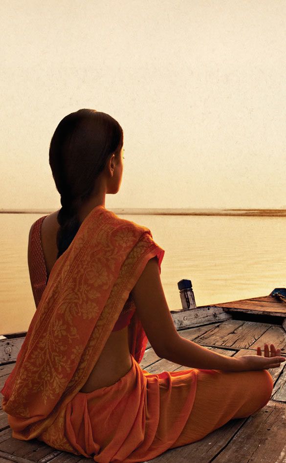 a woman sitting on top of a wooden pier next to the ocean in an orange sari