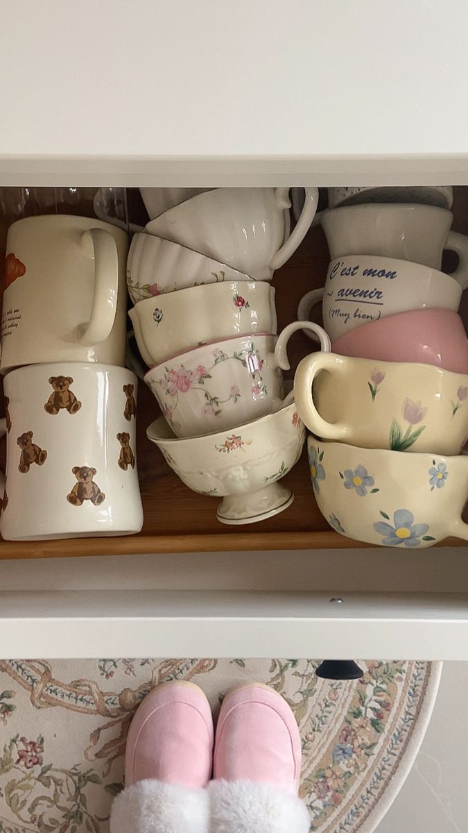 a shelf filled with dishes and cups on top of a table next to a pair of pink slippers