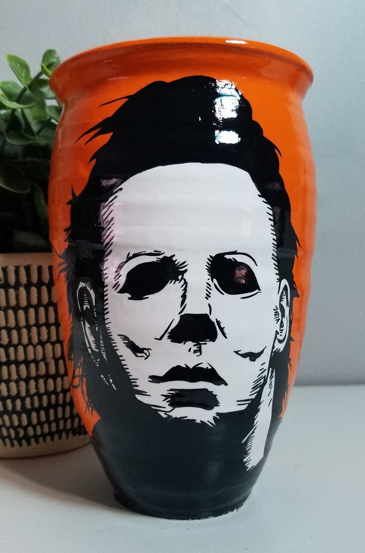 an orange and black pot with a drawing of a man's face on it