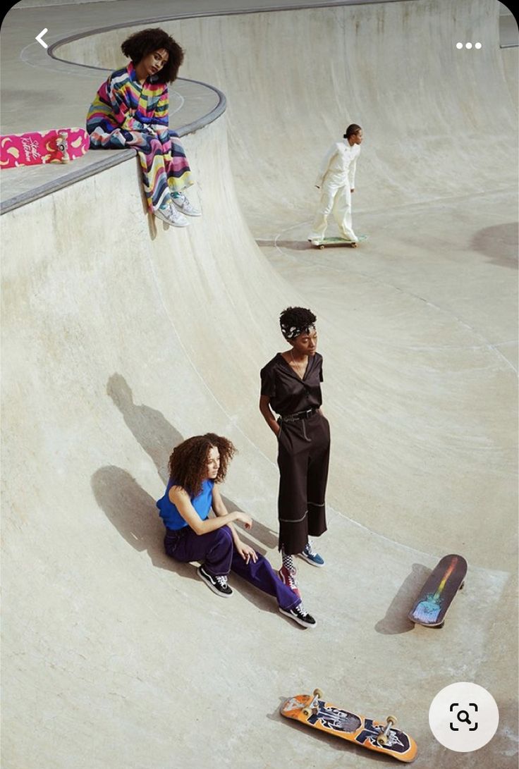 three women sitting on skateboards at a skate park while one woman stands next to her