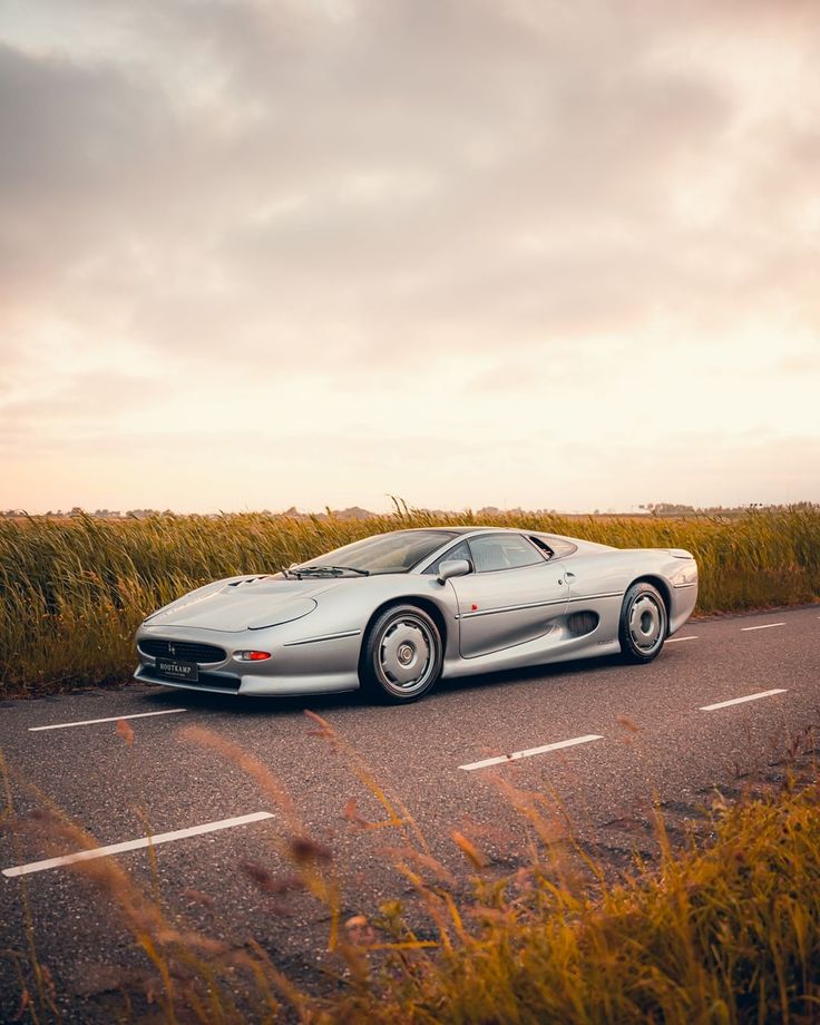 a silver sports car parked on the side of the road in front of tall grass