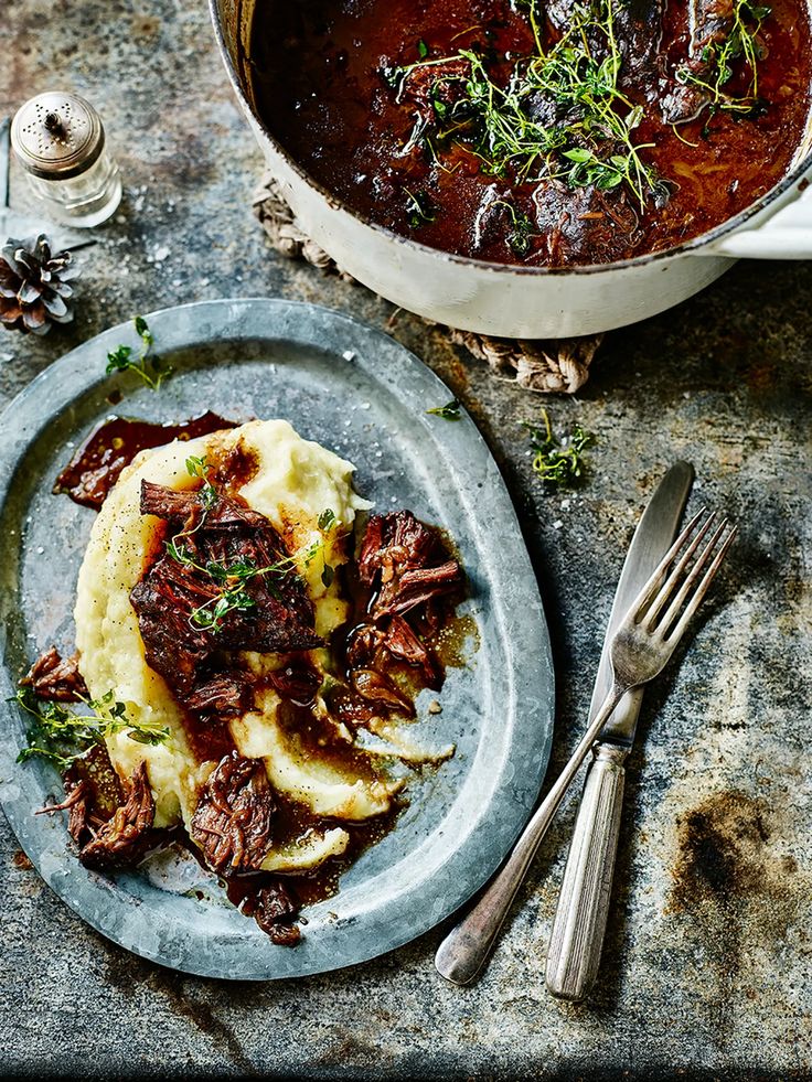 a plate with meat and mashed potatoes on it next to a pot of stew