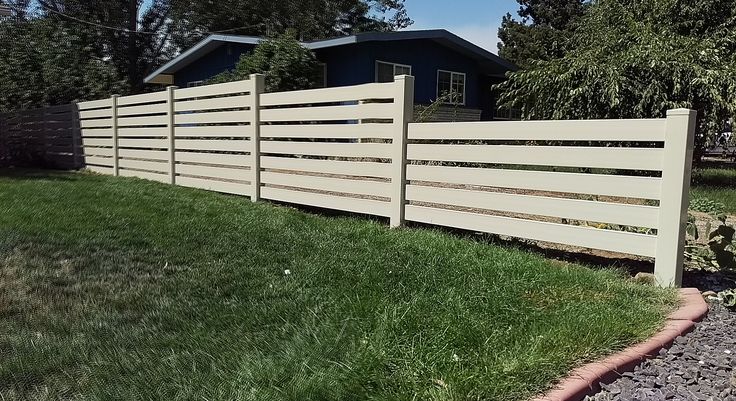 a white fence in front of a house with grass on the ground and trees behind it