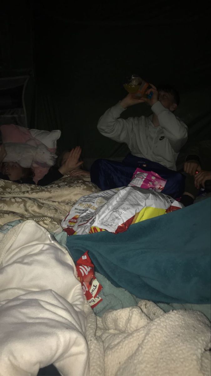 two people are laying on the bed and one person is holding a drink in their hand