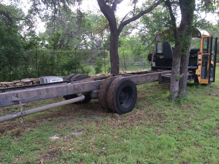 an old tractor trailer is parked in the grass near trees and a bus behind it