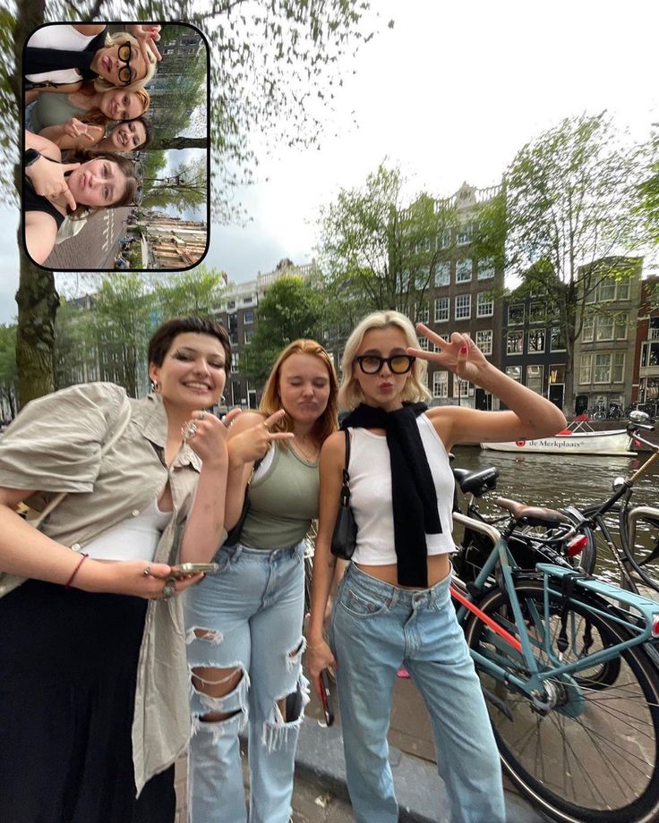 three women standing next to each other in front of some bikes and buildings with their arms around one another