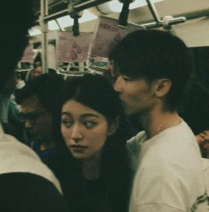 two people standing next to each other on a subway train, one is kissing the other