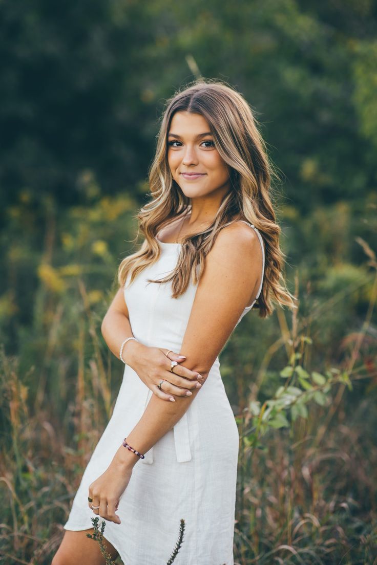 a beautiful young woman standing in tall grass with her arms crossed and smiling at the camera