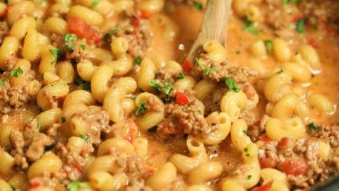 a pot filled with pasta and ground beef in sauce being stirred with a wooden spoon