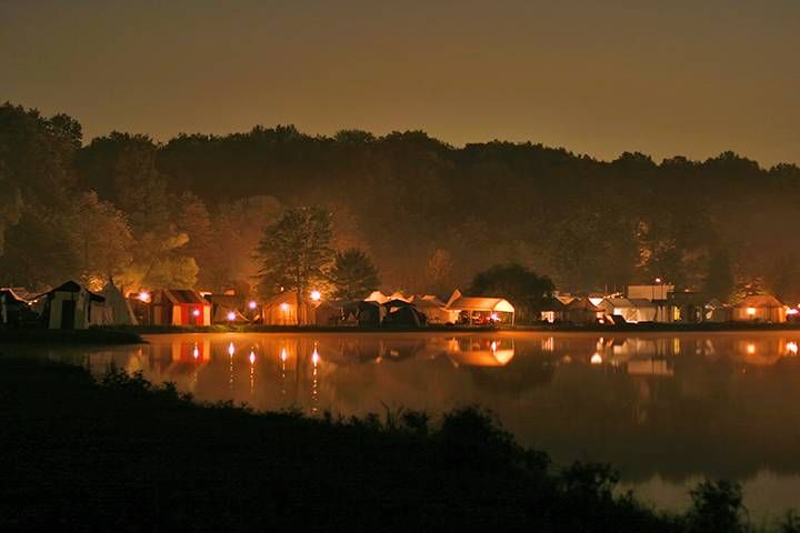 a lake at night with many tents lit up and trees in the backgroud