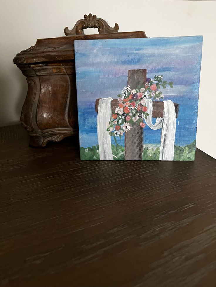 a painting of a cross with flowers on it sitting on a table next to a clock