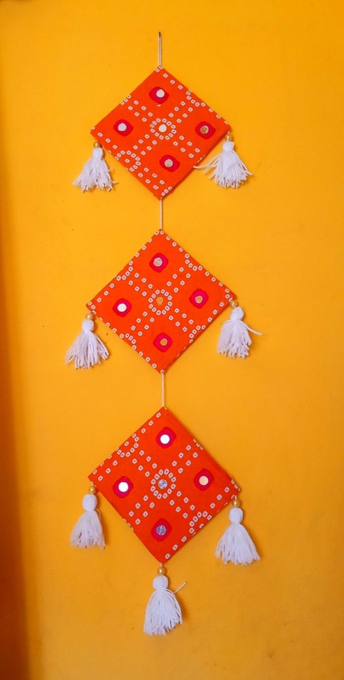 an orange and red wall hanging with white tassels on the top of it