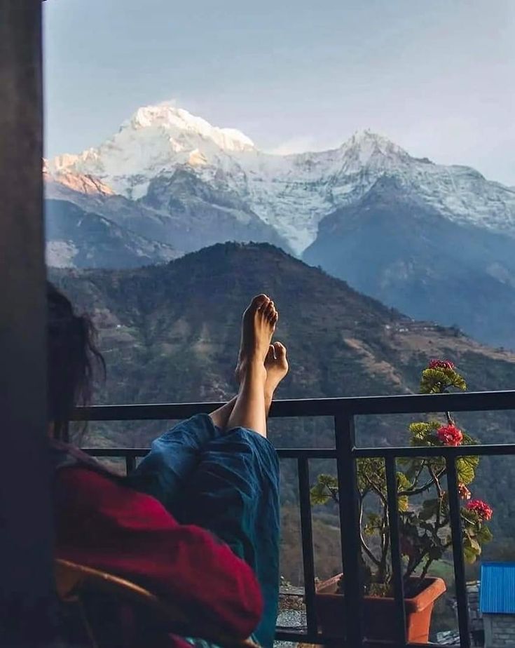 a person is sitting on a balcony with their feet up in the air and mountains in the background