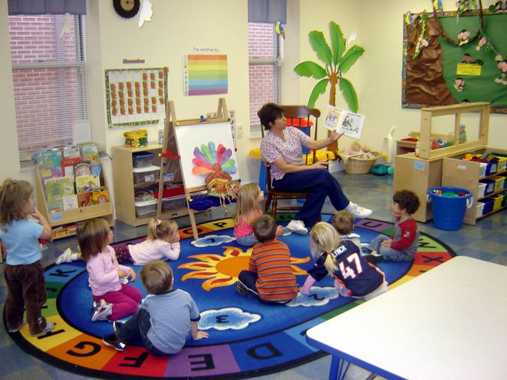 a group of children sitting on top of a colorful rug in a room filled with toys