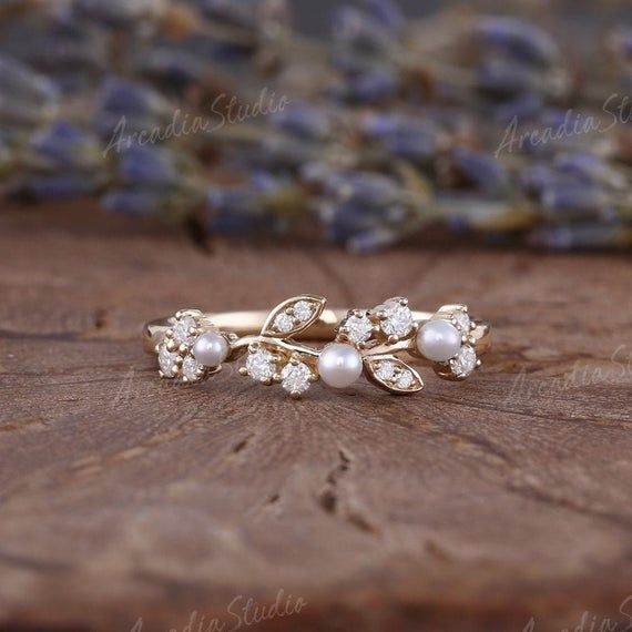 two gold rings with pearls and diamonds on a wooden table next to lavender flowers in the background