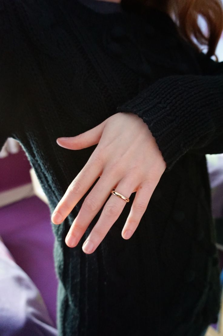 a woman's hand with a gold ring on her left wrist, wearing a black sweater