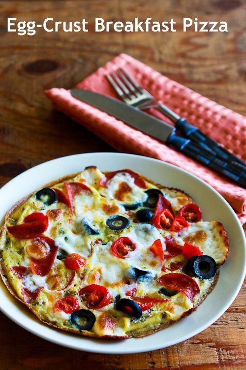 a small pizza with olives, peppers and cheese on a plate next to a fork