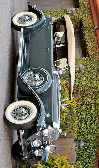 an old car is parked on the side of the road next to some plants and bushes