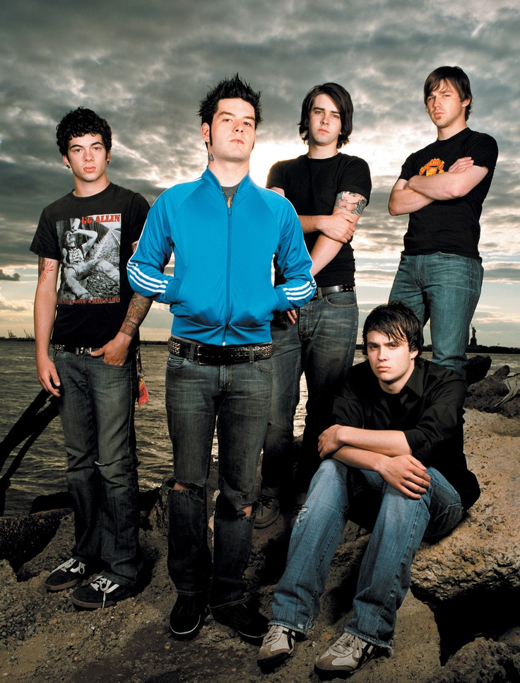 four young men are posing for a photo on the rocks by the water at sunset