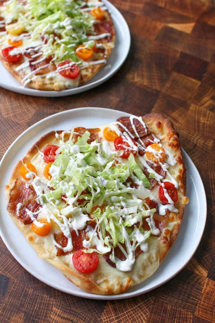 two small pizzas sitting on top of white plates covered in cheese and veggies