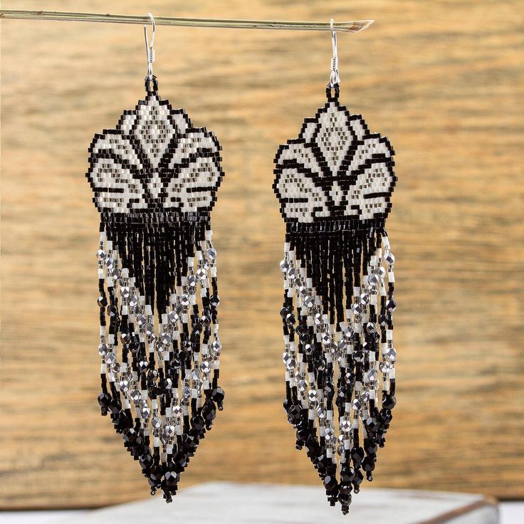 the black and white beaded earrings are hanging from a metal hook on a wooden surface