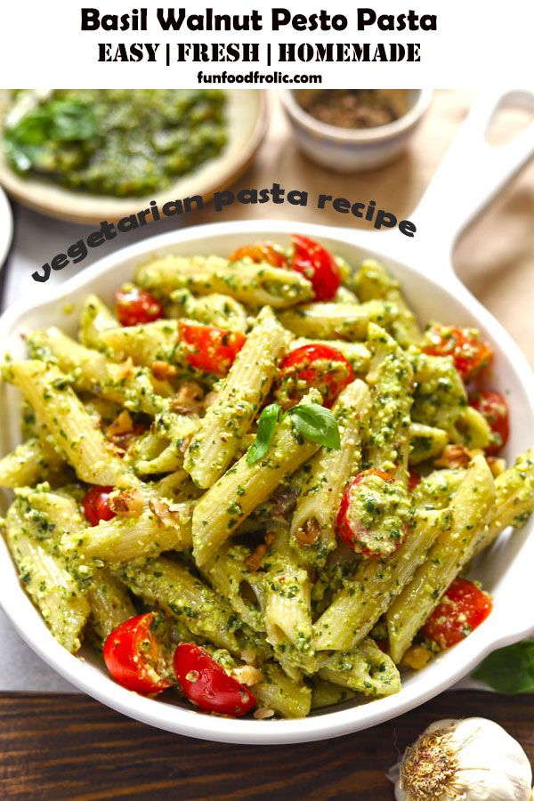 pasta with pesto pesto sauce in a white bowl next to garlic and tomatoes