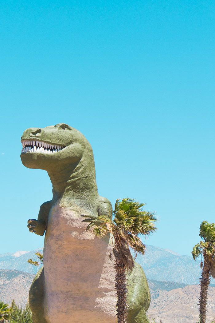 an inflatable dinosaur statue with palm trees and mountains in the background