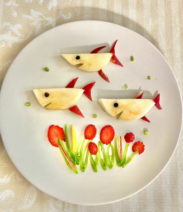 some food is on a white plate with strawberries and other fruit items in the shape of fish