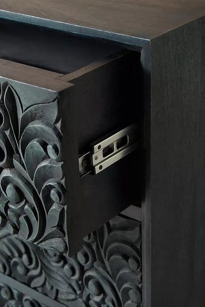 an intricately carved wooden cabinet with metal pulls on the door and drawer, is shown