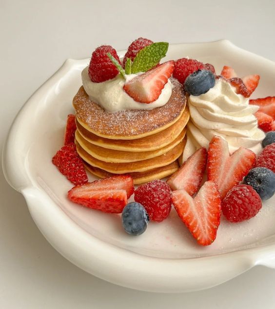 a stack of pancakes topped with whipped cream and strawberries on a white platter