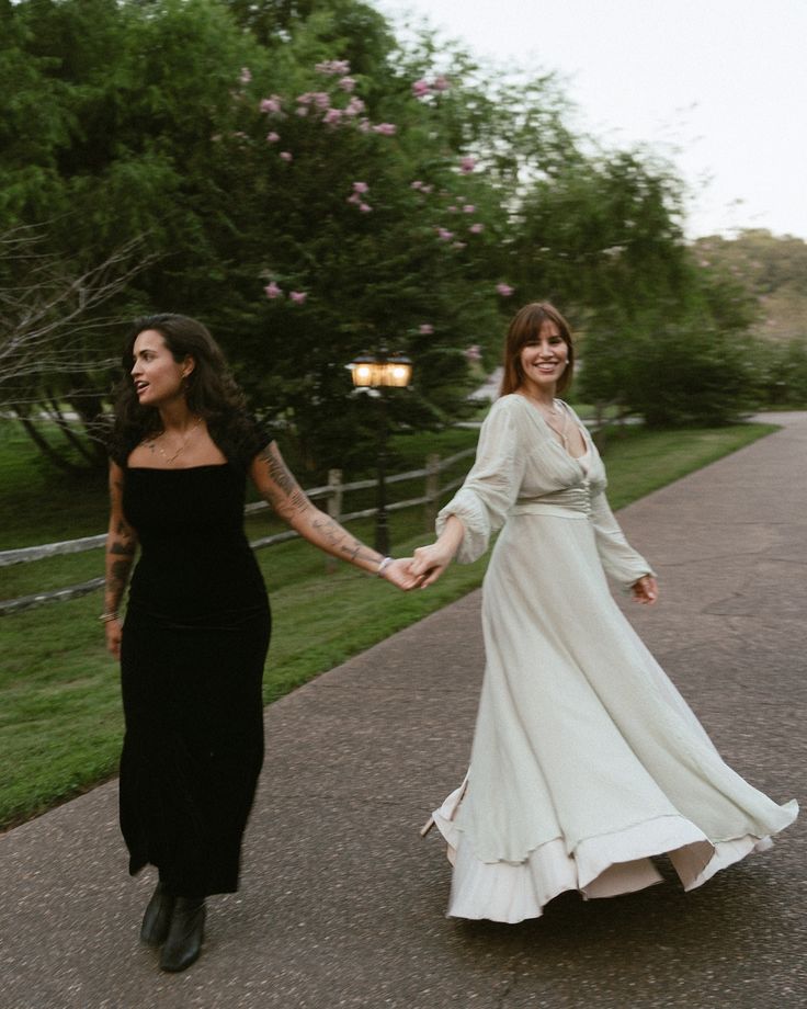 two women are walking down the street holding hands and one is wearing a black dress