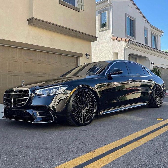 a black mercedes s - class parked in front of a house with garage doors open