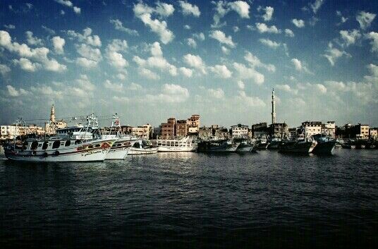 several boats are docked in the water next to some buildings and blue sky with white clouds