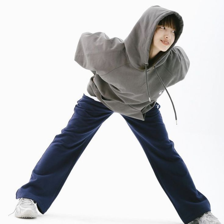 a young man in grey hoodie and blue pants posing with his arms stretched out