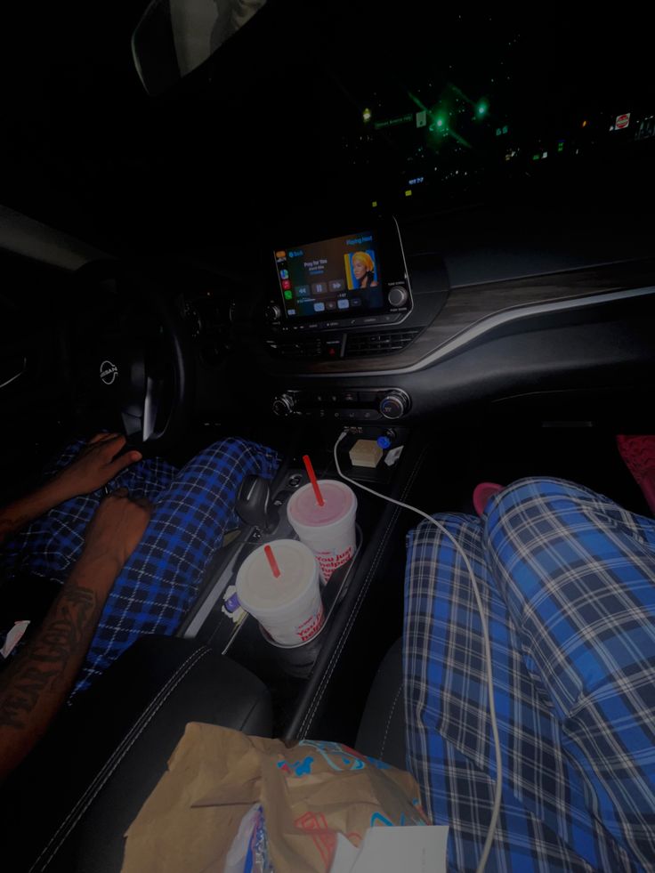 the man is sleeping in his car while using his cell phone and drinking from a cup