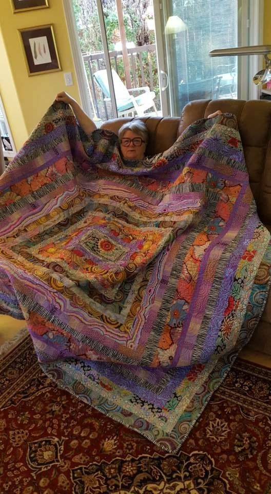 a woman sitting on top of a couch under a colorful blanket in front of a window