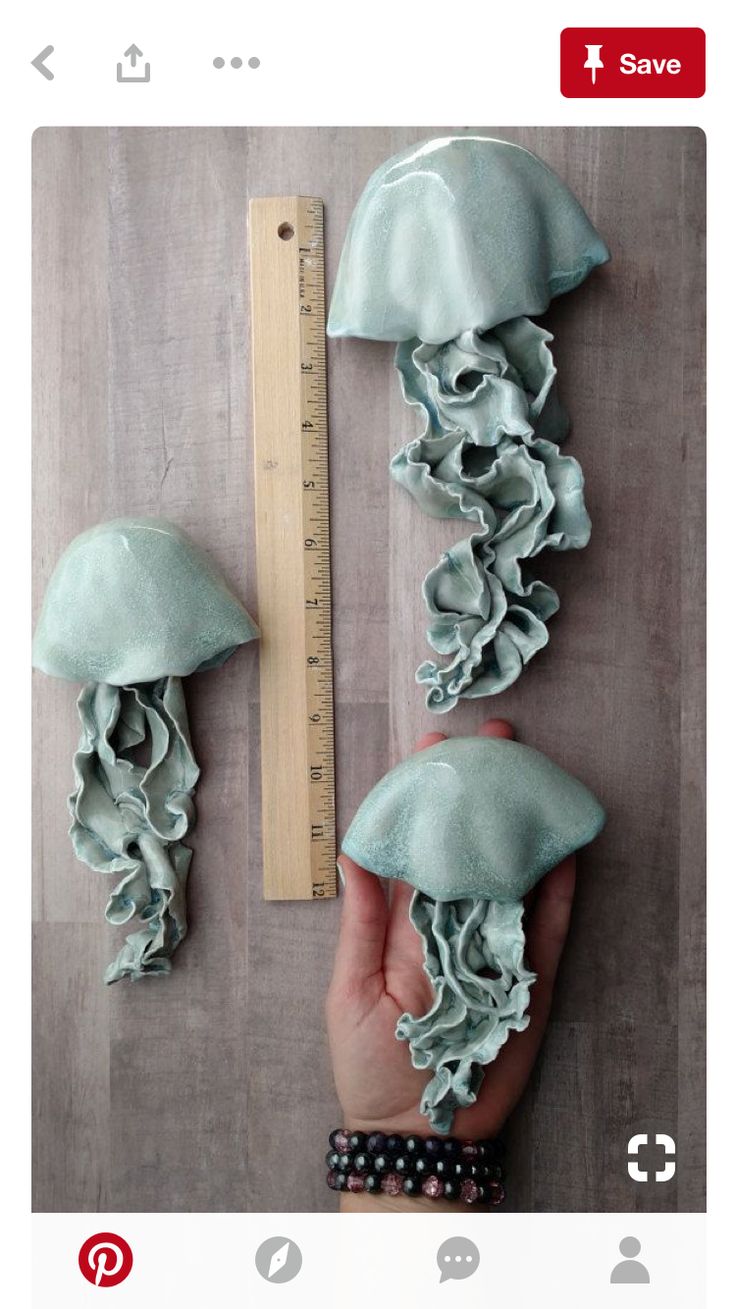 someone is holding their hand up to some jellyfish sculptures on the wall next to a ruler