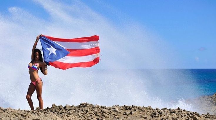 a woman holding an american flag on top of a sandy beach next to the ocean