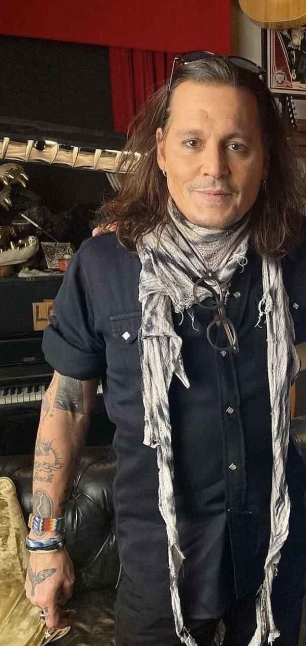 a man with long hair and tattoos standing in front of a guitar case wearing a scarf around his neck