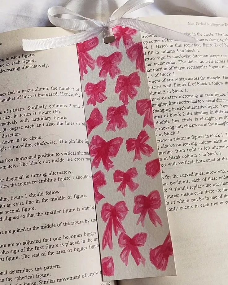 an open book with pink flowers on it and a white ribbon tied around the edge