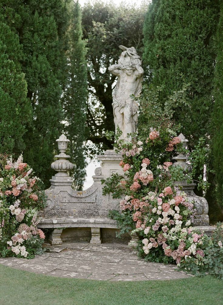 there is a statue in the middle of some flowers and bushes with roses around it