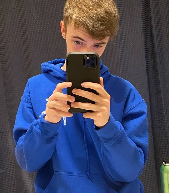 a boy in a blue hoodie is looking at his cell phone and holding it up