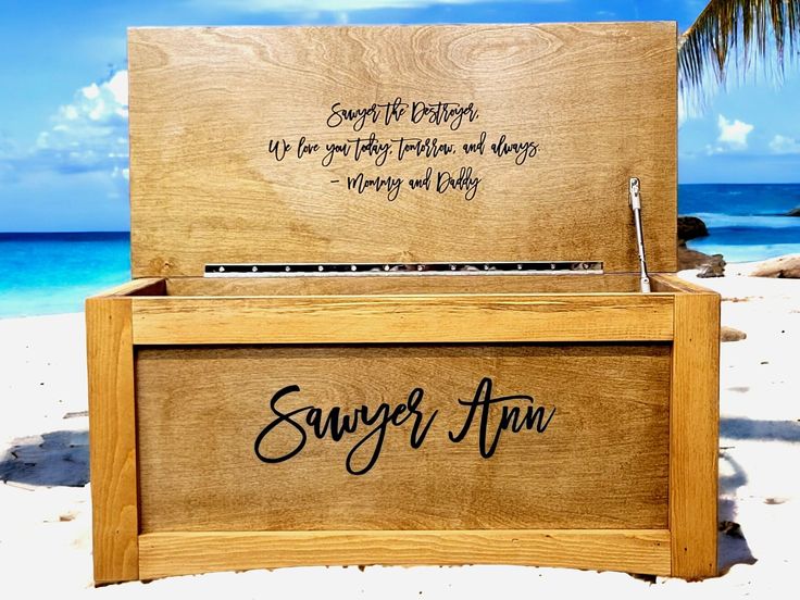 a wooden box sitting on top of a sandy beach next to the ocean with writing on it