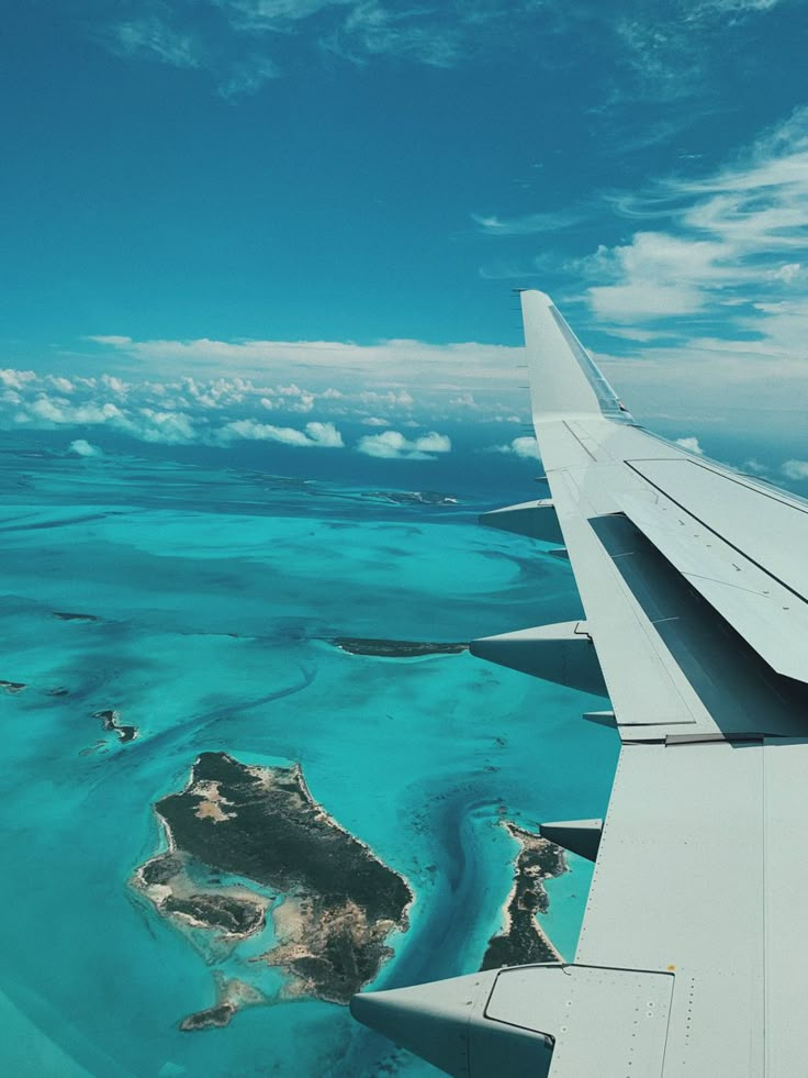 the wing of an airplane flying over water and land in the ocean with blue skies