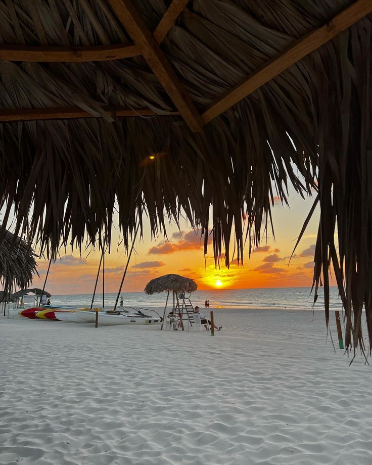 the sun is setting over the beach with palm umbrellas and boats in the water