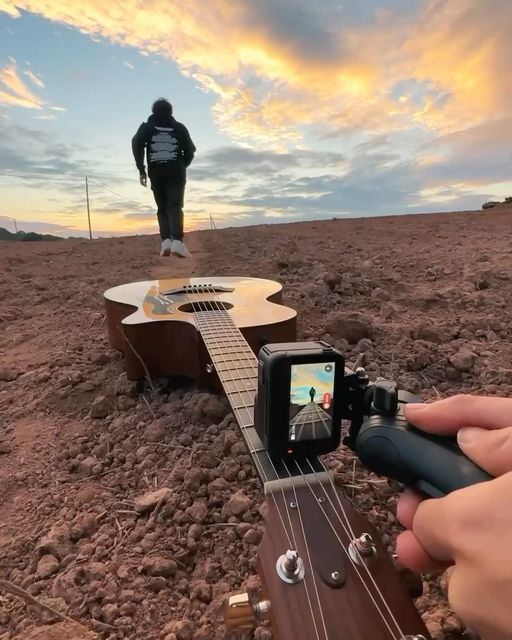 a person holding a guitar in the middle of a field with a camera attached to it