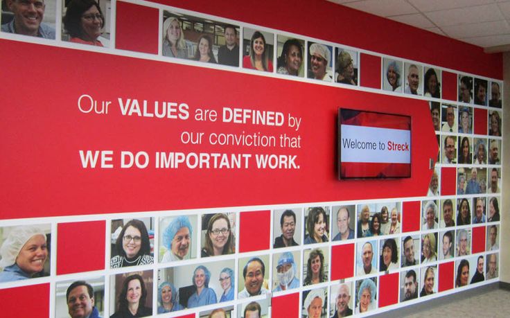 a red wall with many pictures on it and a sign that says our values are defined by our convention that we do important work