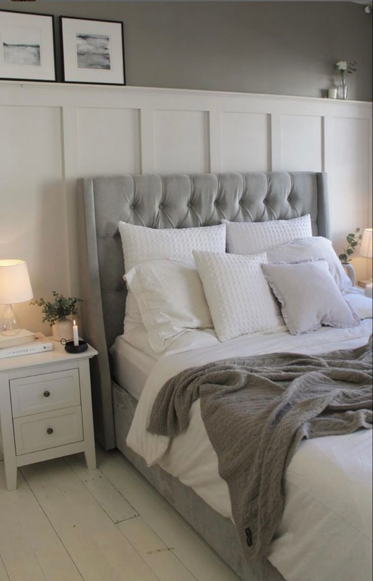 a bed with white linens and gray headboard next to two pictures on the wall